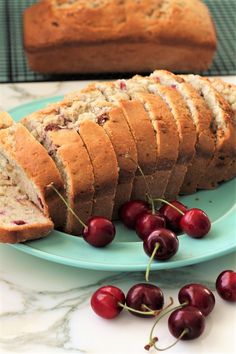 sliced loaf of banana bread with cherries on a plate next to fresh cherries