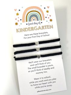 two black cord bracelets with white heart and rainbow in the middle, on top of a card