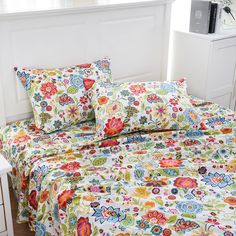 a bed with colorful floral sheets and pillows