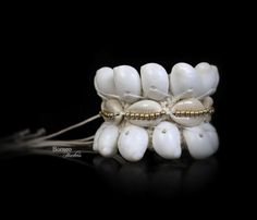 A handwoven white braided rope wide bracelet, decorated with two bands of white curled Shells, a band of cream Cowrie Shells, and a central band of golden round beads. The inner diameter of the bracelet is 2 inches, and the bracelet is 2.1 inches in width. The bracelet is attached by two groups of two, 7.5 inches white cord strands (for adjustable sizing), each decorated at the end with a silver round bead. ► Find these in more dazzling colors here: https://www.etsy.com/listing/231043688/gray-se White Shell Bracelet For Vacation, White Bohemian Shell Bracelet, White Bohemian Beaded Shell Bracelets, Adjustable White Strand Bracelet, White Cowrie Shell Bracelet, White Cowrie Shell Bracelets For Beach, White Beaded Shell Bracelets, White Shell Bracelet, Adjustable White Shell Beaded Bracelet