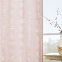 a vase with some flowers in it next to a pink curtain on a window sill