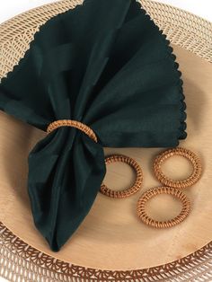 a green napkin and some rings on a wooden plate with wicker placemats