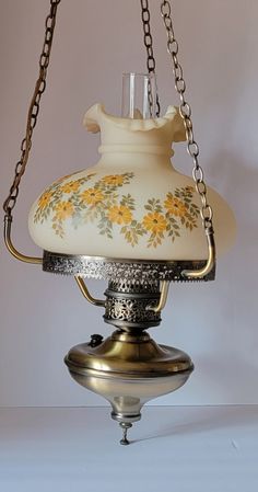 an old fashioned oil lamp hanging from a chain on a white table top with yellow flowers painted on it