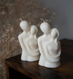 two white candles sitting on top of a wooden table