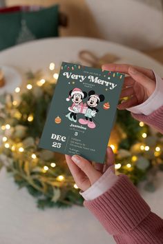 a person holding up a christmas card with mickey and minnie mouse on it