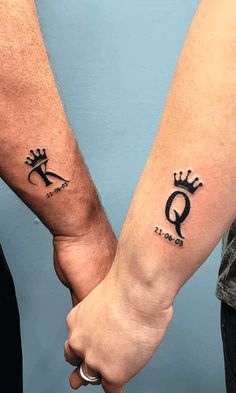 two people holding hands with tattoo designs on their arms, both showing the letter q