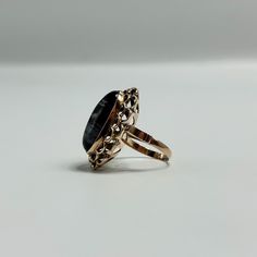 This Vintage 18K Yellow Gold Ring features a stunning oval Snowflake Obsidian gemstone, elegantly set within an ornate filigree setting. The rich, deep black of the gemstone is beautifully contrasted by the delicate white snowflake patterns, creating a striking visual effect. The intricate filigree design adds a touch of timeless elegance and sophistication, making this piece a true statement ring. With a ring size of 6 and a band width of 2.2mm, it offers both comfort and style. Weighing 6.07 grams, this ring is a perfect blend of vintage charm and modern appeal, ideal for collectors or those looking to add a unique piece to their jewelry collection. Snowflake Patterns, Snowflake Obsidian, 18k Yellow Gold Ring, White Snowflake, Filigree Design, Snowflake Pattern, Deep Black, Yellow Gold Ring, Yellow Gold Rings