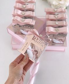 a person is holding a card in front of some pink boxes with bows on them