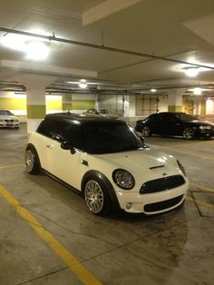 a white mini cooper parked in a parking garage with two black cars behind it and yellow lines on the floor