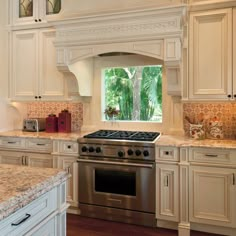 a kitchen with white cabinets and marble counter tops, an oven and stove top in front of a window