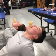 two men are laying on the floor with ice cream cones in their mouths and one has his eyes closed