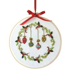 a christmas ornament hanging from a red ribbon on a white hoop with holly and bells