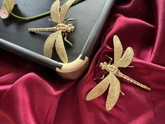 two gold dragon brooches sitting on top of a red cloth next to each other