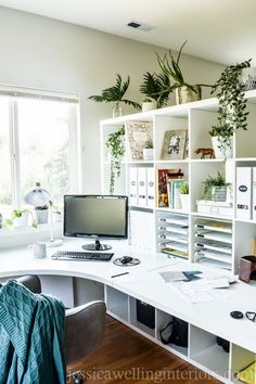 a white desk topped with a computer monitor next to a plant filled window sill