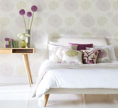 a white bed sitting next to a wooden table with flowers on it and two vases