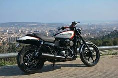 a motorcycle parked on the side of a road near a fence and cityscape