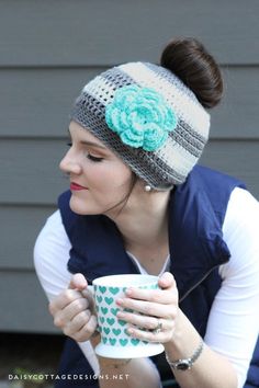 a woman is holding a coffee cup and wearing a knitted headband with a flower on it