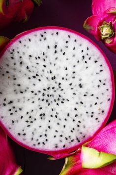 a dragon fruit cut in half and surrounded by other fruits on a purple tablecloth