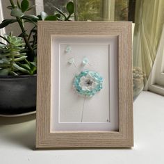 a white and blue flower in a frame on a table next to a potted plant