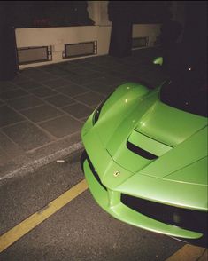 the green sports car is parked on the side of the road at night, with no one around it