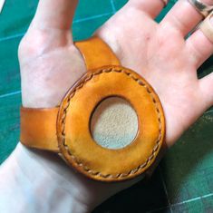 a person's hand with a leather wristband and ring in the middle, on top of a green surface