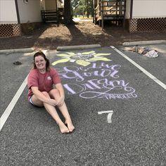 a woman is sitting on the ground in front of chalk drawings that spell out her name