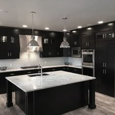 a large kitchen with black cabinets and stainless steel appliances, including an island in the middle