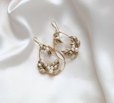 These handcrafted antique gold wedding earrings showcase a boho-inspired floral design, featuring delicate leaves and freshwater pearls. Expertly made to order, these hoop earrings add a touch of elegance and uniqueness to any bridal look. - Handcrafted in my PA studio - Genuine Austrian golden shadow crystal rock fabric leaves - Freshwater pearls - Antique gold leaves  - Available in rose gold, yellow gold or rhodium (silver) - Earrings measure 2.5 inches x 1-5/8 inch - Handcrafted in the US. - Nickel free and hypoallergenic - PLEASE ALLOW APPROX 10 BUSINESS DAYS FOR COMPLETION BEFORE SHIPPING. This is an original design by © Treasures by Agnes Browse our earrings: https://www.etsy.com/shop/treasures570?ref=seller-platform-mcnav&section_id=6861728 Browse our backdrop necklaces: https://ww Gold Earrings With Intricate Design For Wedding, Vintage Dangle Flower Earrings For Wedding, Gold Brass Hoop Earrings For Wedding, Delicate Brass Wedding Earrings, Yellow Gold Brass Earrings For Wedding, Brass Filigree Hoop Earrings For Wedding, Vintage Gold Pearl Earrings For Wedding, Elegant Brass Hoop Earrings For Wedding, Delicate Gold Hoop Earrings For Wedding