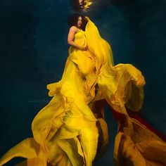 a woman in a yellow dress under water with her arms wrapped around her body and head