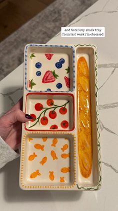 a person holding three plates with fruit designs on them, one is empty and the other has food in it