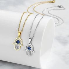 Featuring a delicate Hamsa Hand pendant adorned with sparkling cubic zirconia stones and a captivating evil eye, this necklace is a symbol of good luck, health, and happiness.  What's Included: 1 x Necklace or Necklace Set of 2 Pendant Size: 1cmx1.5cm Key Features: *Symbolic Design: Combines the protective power of the Hamsa Hand and Evil Eye *Sparkling Cubic Zirconia: Adds a touch of glamour and elegance *Gold/Silver Finish: Choose the perfect metal to match your style *Delicate Chain: Creates Silver Cubic Zirconia Charm Necklaces, Tarnish Resistant, Silver Tarnish Resistant Charm Necklaces With Cubic Zirconia, Silver Cubic Zirconia Charm Necklaces For Jewelry Making, Silver Spiritual Necklace With Cubic Zirconia, Spiritual Silver Cubic Zirconia Necklace, Spiritual Silver Necklace With Cubic Zirconia, Silver Crystal Charm Necklaces For Jewelry Making, Silver Pendant Necklace With Diamond Eyes, Silver Metal Jewelry With Evil Eye