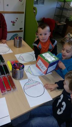 four children sitting at a table with paper and colored pencils in front of them