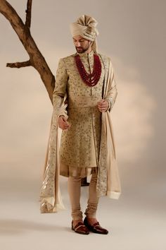 Sandune Sherwani Set | Jatin Malik Introducing our exquisite sand grey all-over hand-embroidered sherwani set, a true work of art. The foundation of this sherwani is crafted with golden zari threads, creating a luxurious base texture. The second tier is highlighted with intricate gold dabka work, accentuating the overall brilliance. This ensemble is perfectly complemented by a tone-on-tone hand-embroidered stole and safa, adding an extra layer of elegance and sophistication. Perfect for making a grand statement, this sherwani set embodies opulence and refined craftsmanship. Included in purchase: Sherwani, Kurta, Churidar, Stole, Safa, Cummerbund Product Specification Color: Sand grey Fabric: Linen silk Occasion: Engagement, Wedding, Bridal, Reception Style: Sherwani, Kurta, Churidar, Safa, Gold Sherwani With Zari Work For Designer Wear, Gold Sherwani With Resham Embroidery And Kundan, Jamawar Sherwani With Zari Work For Reception, Traditional Beige Raw Silk Sherwani, Gold Sherwani With Zari Work In Kundan, Gold Sherwani With Dupatta In Raw Silk, Gold Raw Silk Sherwani With Zari Work, Beige Raw Silk Sherwani With Zari Work, Gold Traditional Wear With Naqshi Drape