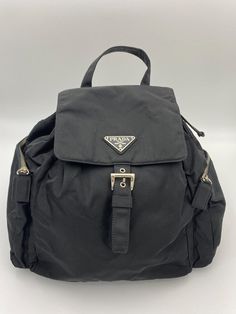 This vintage cult backpack from Prada is the ultimate throwback bag. When Prada released its original nylon backpack in 1984 it was an instant hit. This nylon backpack with a modern, minimalist design is decorated with the Prada enamel triangle logo. Underneath the flap with a leather strap and buckle, is a drawstring closure. There are two adjustable webbing shoulder straps with Prada branded buckles. There are two side zip pockets on the outside. Inside features the iconic Prada logo lining an Modern Minimalist Design, Prada Nylon, Prada Logo, Logo Line, Handbag Wallet, Triangle Logo, Wallet Accessories, Diaper Backpack, Vuitton Bag