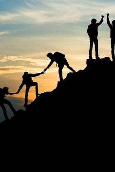 four people holding hands on top of a mountain with the sun setting in the background