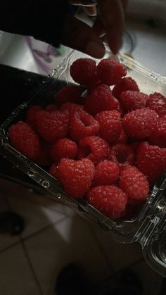 raspberries in a plastic container being held by someone's hand over the counter