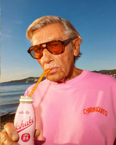 an old man with sunglasses and a pink shirt is holding a drink in his hand