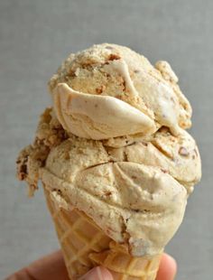 a hand holding an ice cream cone with pecans on top