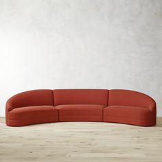 an orange curved sofa sitting on top of a hard wood floor next to a white wall