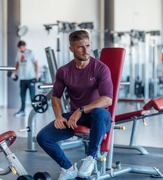 a man sitting in a gym chair with his feet on the barbells and looking at the camera