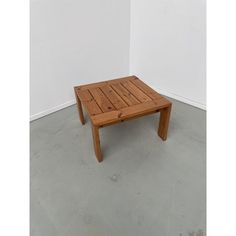 a small wooden table sitting on top of a cement floor next to a white wall