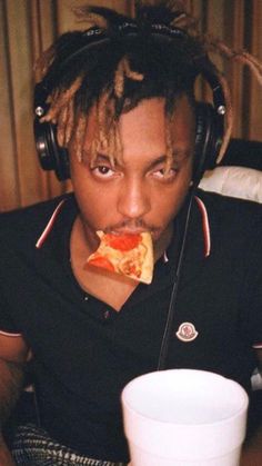 a young man with headphones eating pizza and drinking from a white cup in front of him