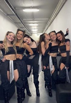 a group of women standing next to each other in front of a white wall wearing black outfits