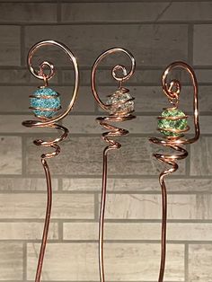 three metal sculptures with different colored beads on them in front of a brick wall ornament