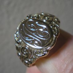 Such a beautiful ring for they guys but could be sized down for the ladies, within reason. This ring has fabulous scroll detailing on the shoulders. The oval face area is approx. 5/8 inches long and under 1/2 inch wide. Marks are the back 10 k and tested as such. Ring is heavy at 8.8 grams and approx. a size 13. This ring has been size up in the past. You can feel a slight ripple in the band in back as well as it being a bit thinner. Not an issue but an observation. The initials on the face look Heirloom Engraved Ring Jewelry, Classic 14k Gold Engraved Ring With Intricate Design, Luxury Oval Signet Ring With Intricate Design, Luxury Signet Ring With Intricate Design For Anniversary, Classic Intricate 14k Gold Jewelry, Silver Heirloom Initial Ring For Wedding, Formal Silver Initial Ring Stamped 14k, Vintage White Gold Jewelry With Engraving Option, Engraved Victorian 14k Gold Jewelry