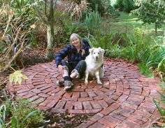 a woman sitting in the middle of a brick path with her white dog on it