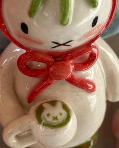 a ceramic cat figurine with a red bow around its neck and eyes, holding a green object in it's hand