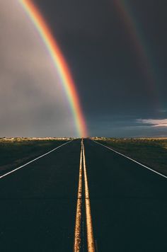 two rainbows are in the sky over an empty road with no cars on it