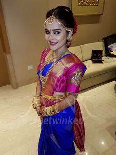 a woman in a blue and pink sari with gold jewelry on her head, standing next to a couch