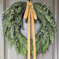 a green wreath with yellow ribbon hanging on a wooden door, decorated with white flowers and greenery